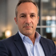 Portrait de Gaelig Drouin, en veste sombre et chemise bleu clair, dans les bureaux de L’Administrateur
